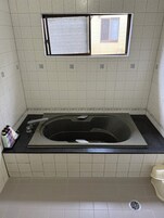 Un baño con bañera, ventana y pared con azulejos.