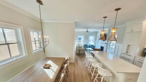 A spacious kitchen with a wooden dining table, white bar stools, and pendant lighting.