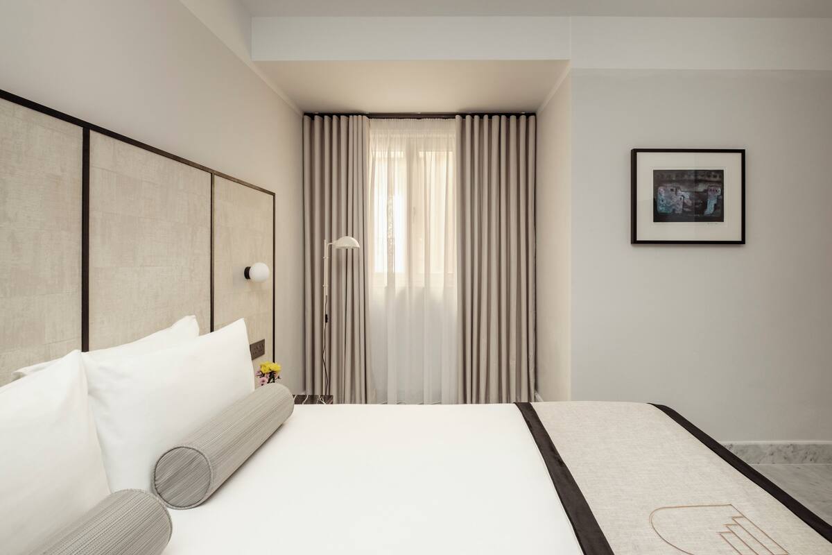 Una habitación de hotel moderna con una cama grande, una mesita de noche, una lámpara y un cuadro enmarcado en la pared.