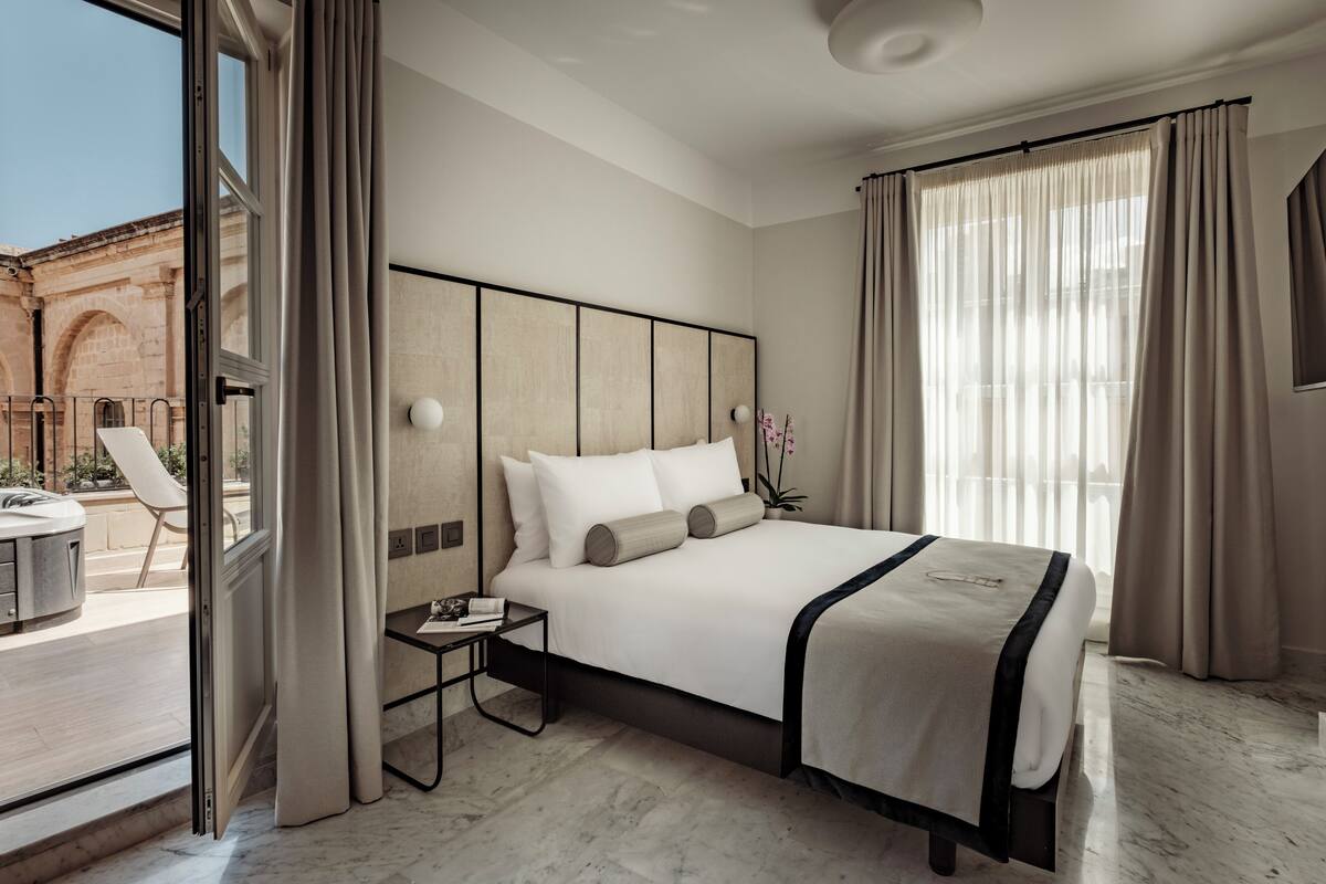 Habitación de hotel moderna con una cama grande, una mesita de noche y vistas al exterior.