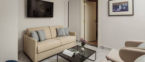 A modern living room with a beige sofa, a glass coffee table, a flat-screen TV, and a framed picture on the wall.