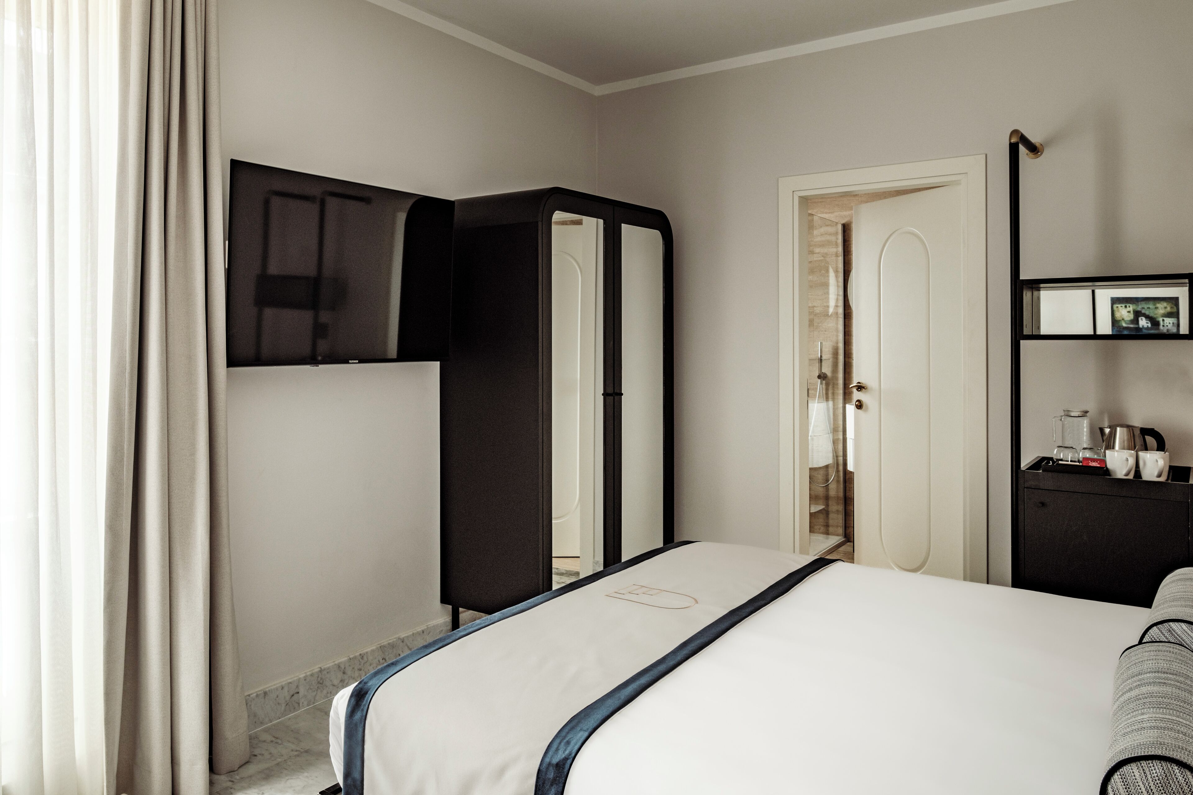 Una habitación de hotel con cama, armario, espejo, puerta y una mesita con objetos encima.
