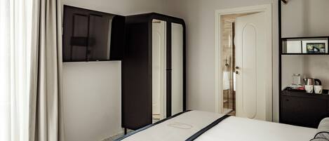 Una habitación de hotel con cama, armario, espejo, puerta y una mesita con objetos encima.