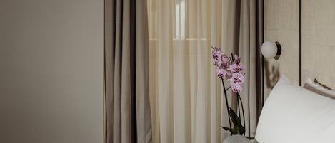 Habitació d'hotel amb un llit, una petita taula de nit, una làmpada i una finestra amb cortines translúcides.