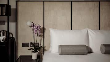Habitación de hotel ordenada con cama, almohadas, mesita de noche con lámpara y planta en maceta.