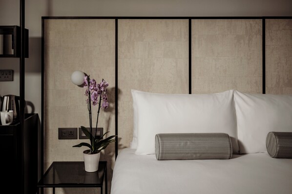 A neatly arranged hotel room with a bed, pillows, a bedside table with a lamp and a potted plant. - San Karlu Hotel (Valletta)