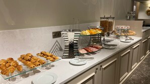 Een ontbijtbuffet met diverse soorten eten, zoals gebak, kazen en vleeswaren.