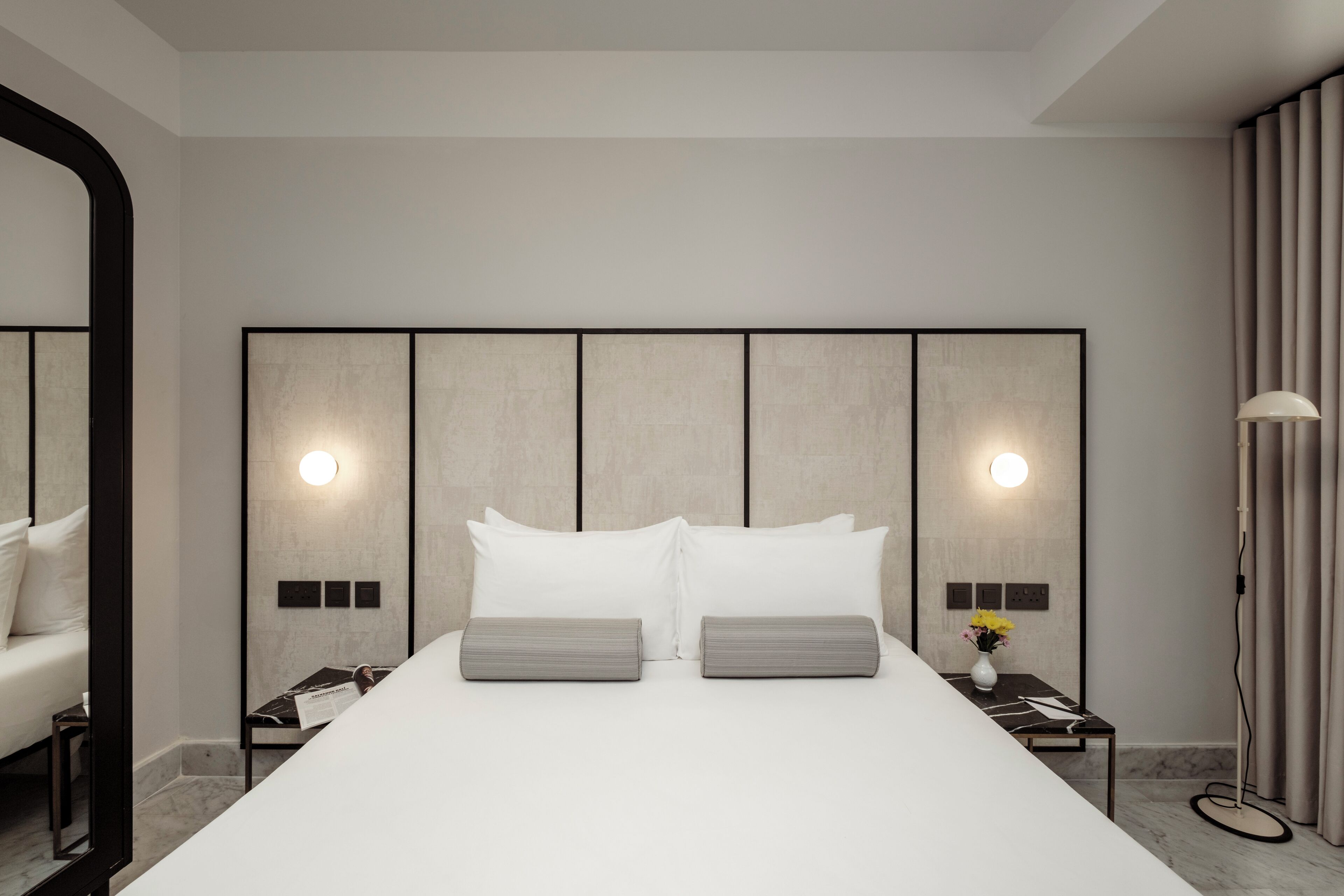 Una habitación de hotel moderna con una cama grande, dos mesitas de noche, una lámpara de pie y un espejo.