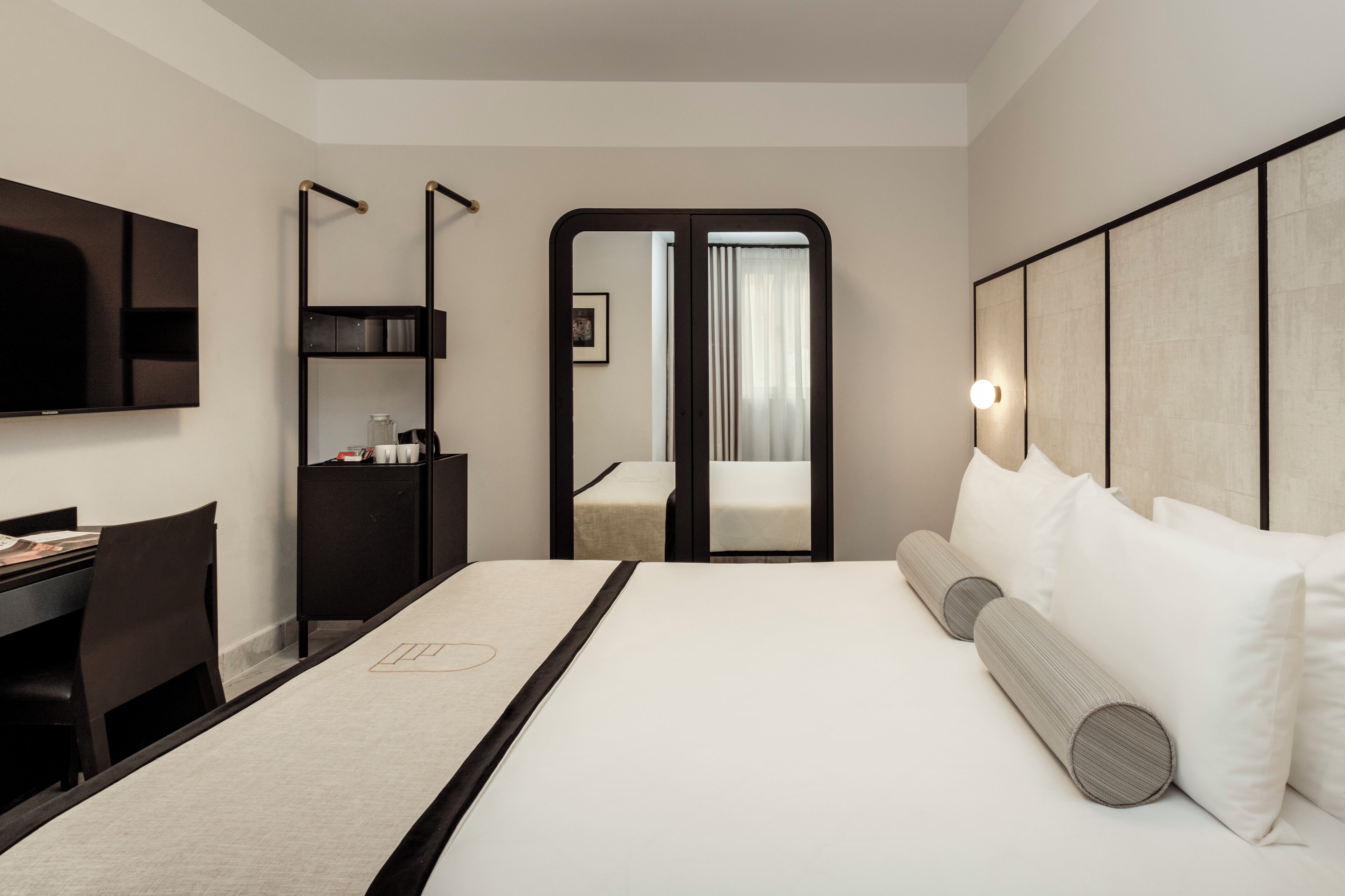 A modern hotel room with a large bed, a desk, and a wardrobe.