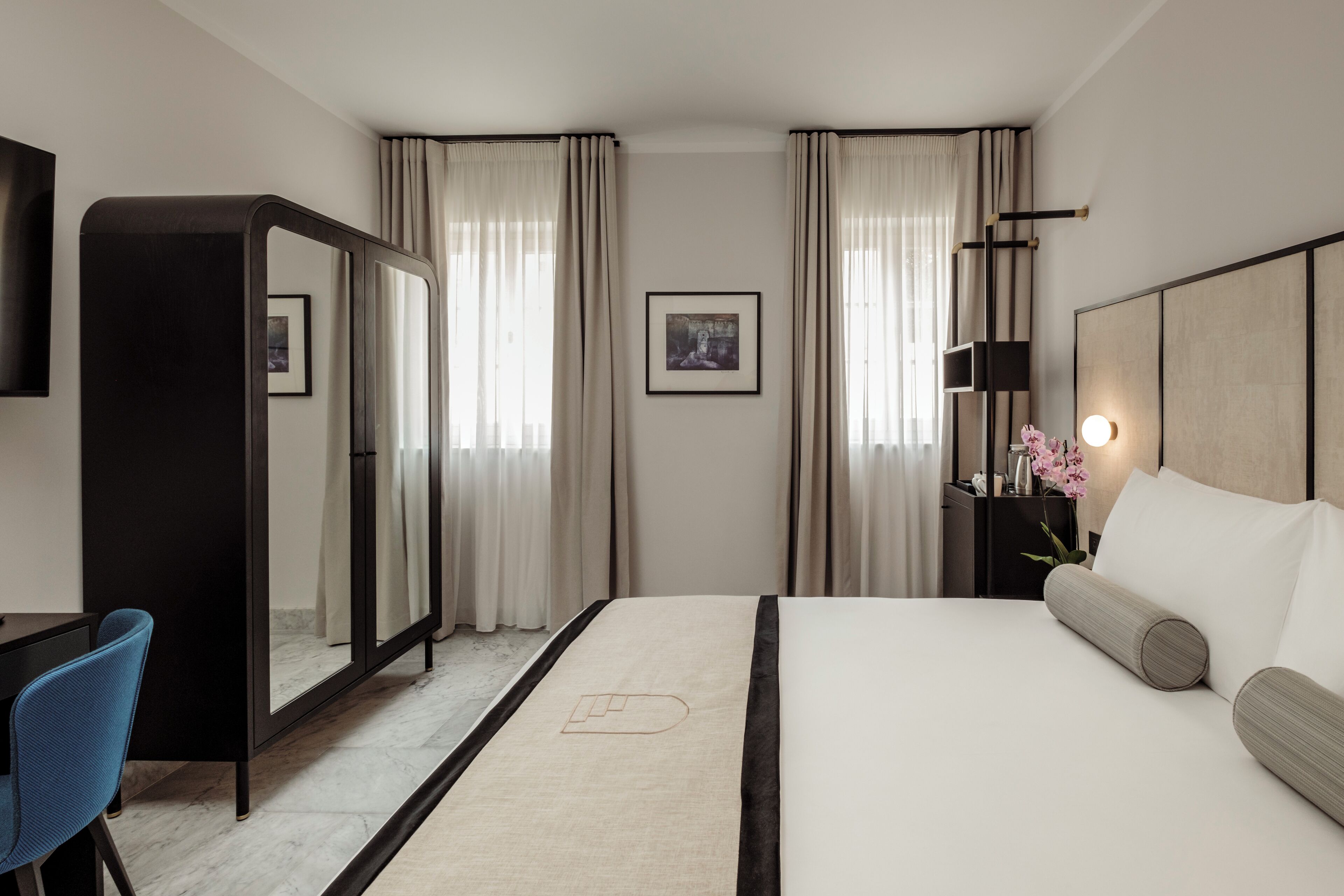 Una habitación de hotel con cama, escritorio, silla, espejo y cortinas.