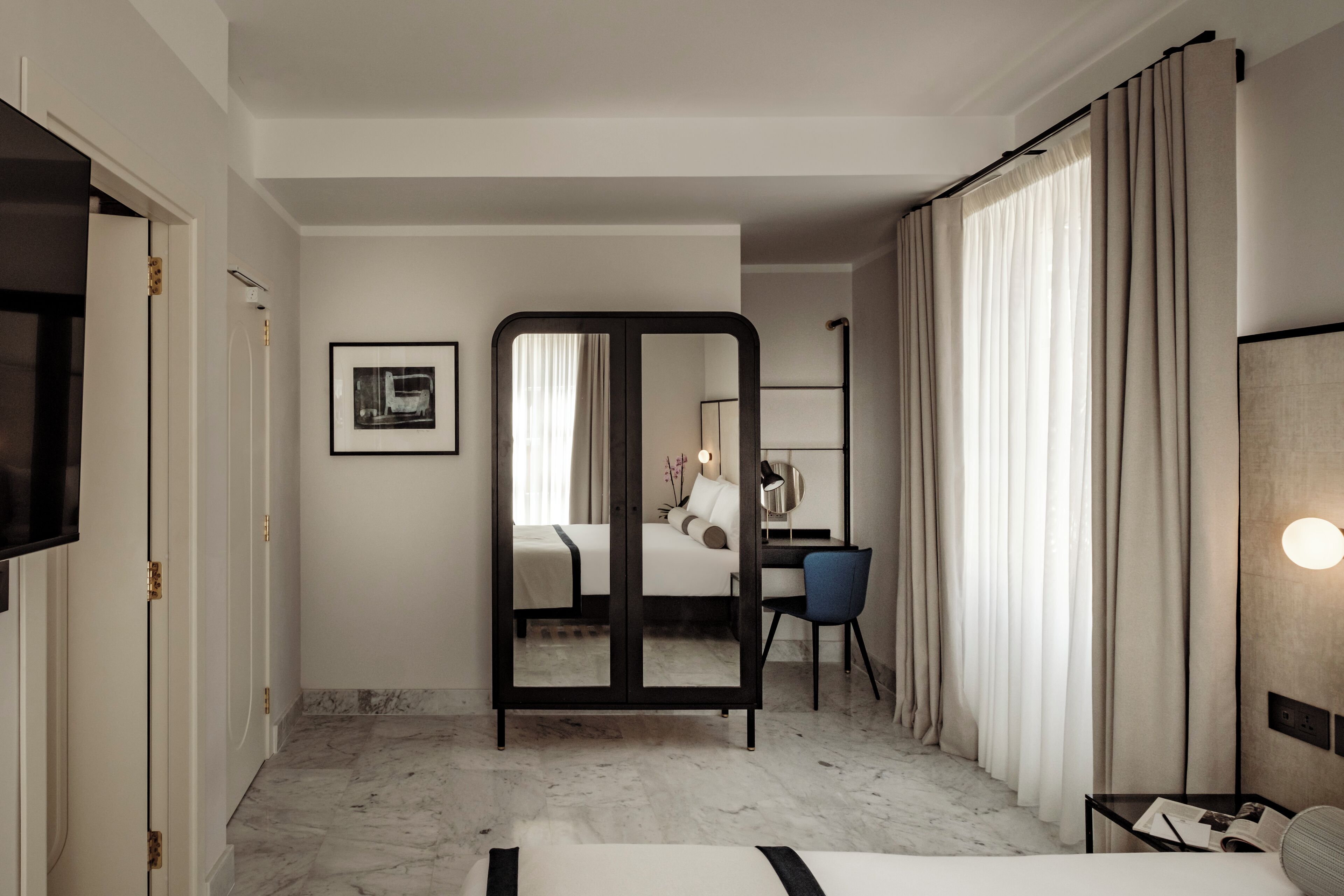 A hotel room with a bed, a desk, a chair, a mirror, and a wardrobe.