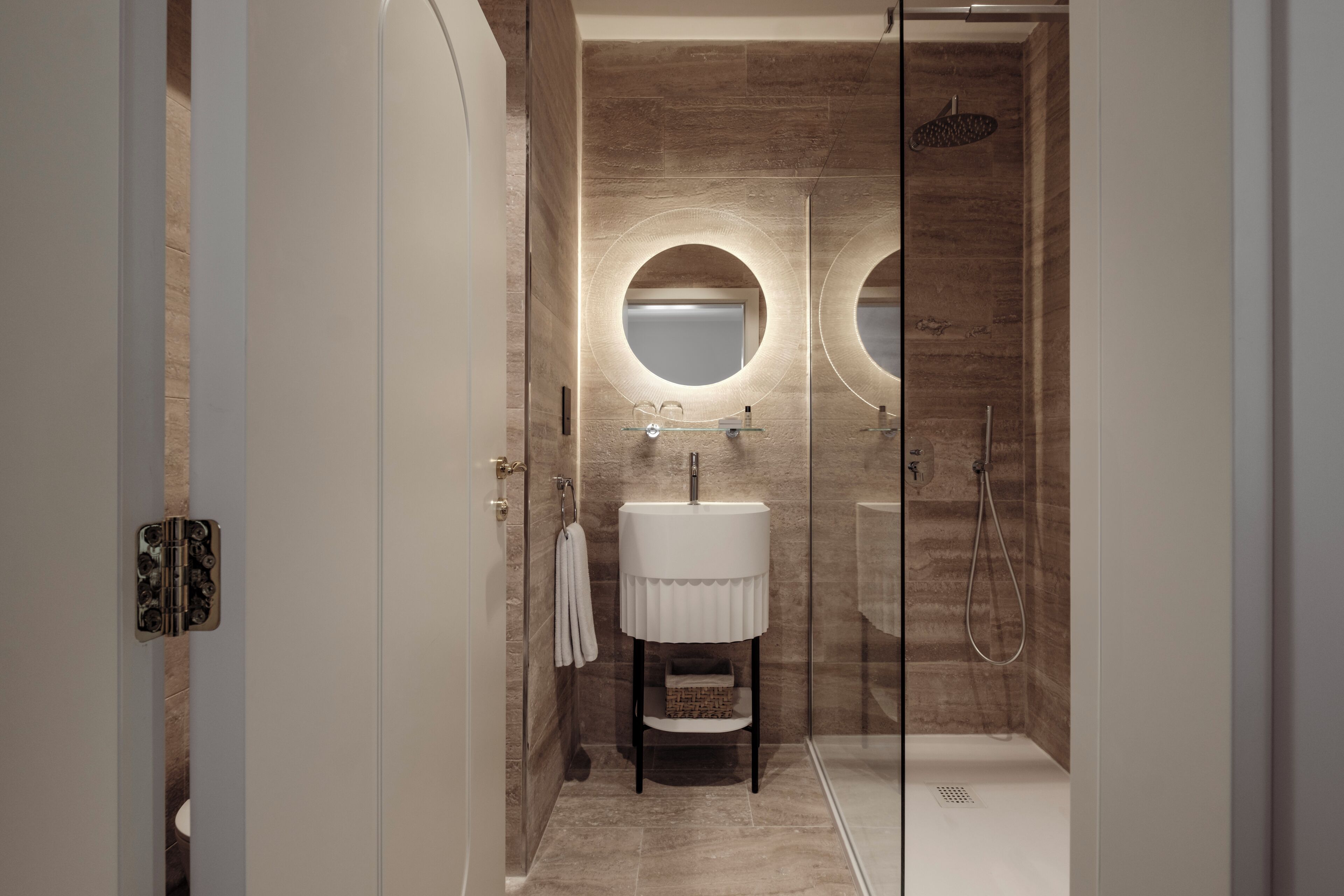 A modern bathroom with a glass shower enclosure, a white pedestal sink, and two round mirrors.