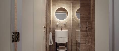 A modern bathroom with a glass shower enclosure, a white pedestal sink, and two round mirrors.
