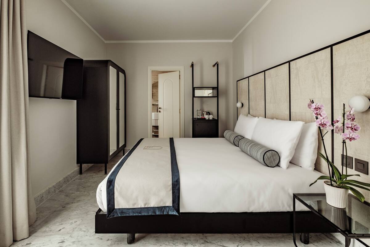 Una habitación de hotel moderna con una cama grande, televisión, armario, mesita de noche y una orquídea en maceta.