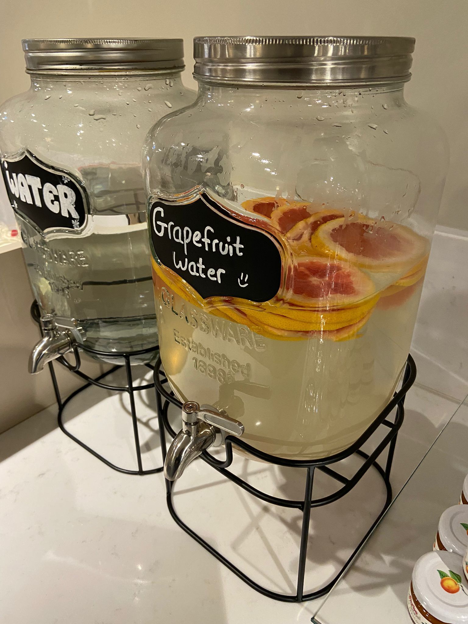Twee glazen potten op een metalen standaard, waarvan één 'Water' en de andere 'Grapefruitwater' is aangeduid.