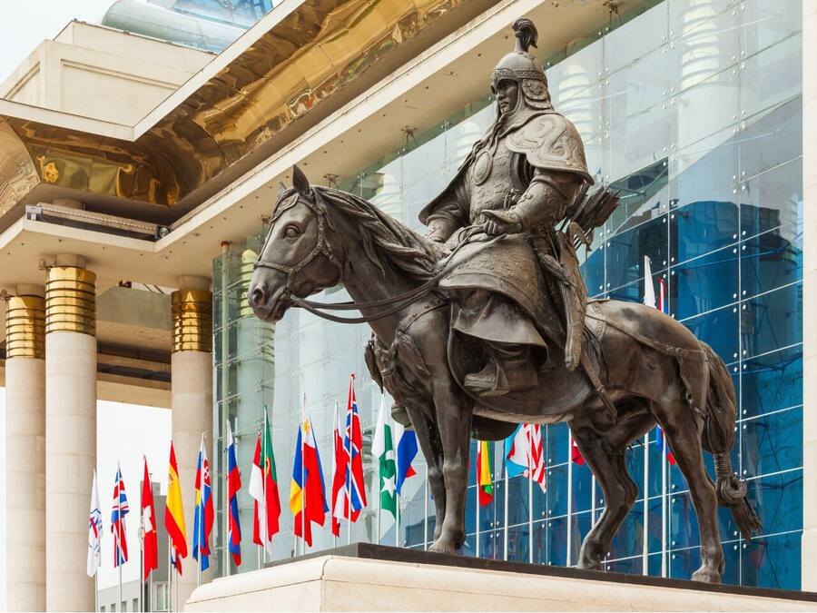 Una estatua de un jinete frente a un edificio con columnas y banderas.