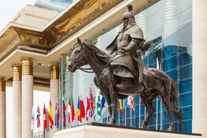 Una estatua de un jinete frente a un edificio con columnas y banderas.