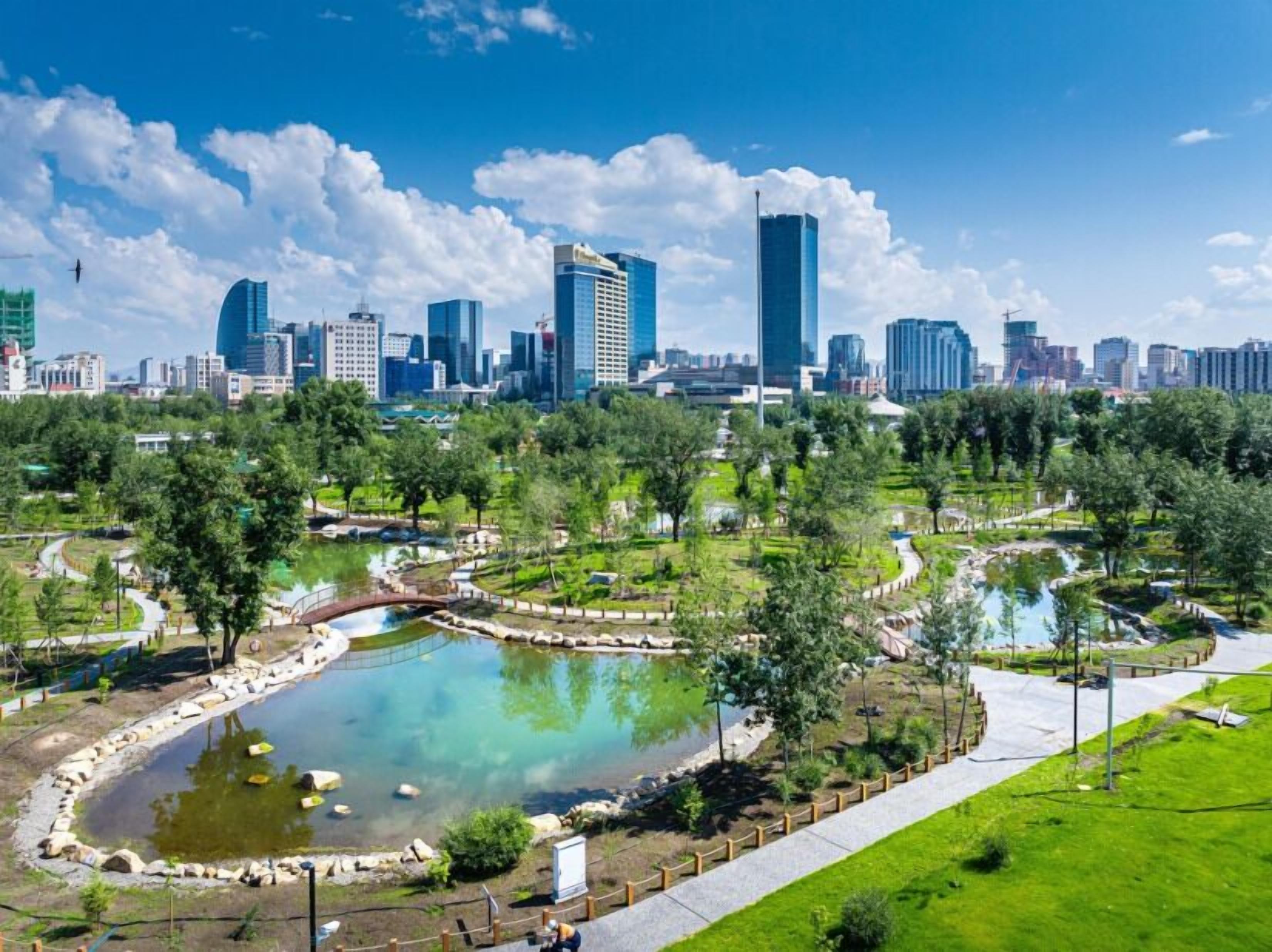 A cityscape with modern skyscrapers and a park with a pond.