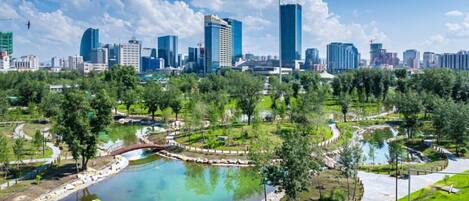 A cityscape with modern skyscrapers and a park with a pond.