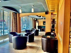 En moderne lobby med læderpolstrede møbler, en receptionsdisk og store vinduer med udsigt over byen.