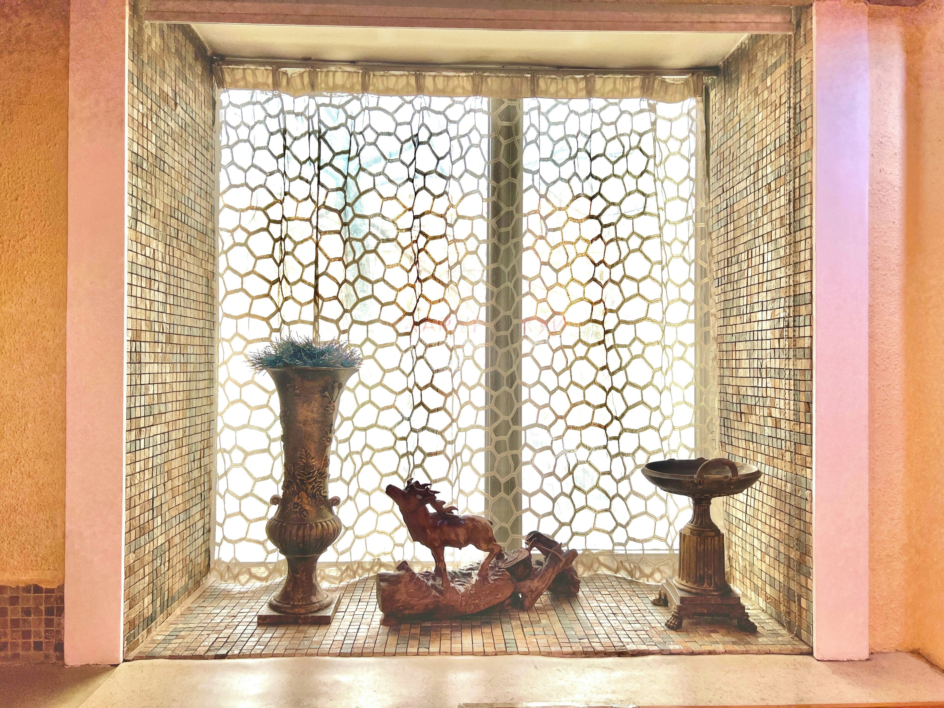 Una habitación con piso de baldosas, un ventanal decorativo con un diseño geométrico y dos jarrones con una figurita de caballo entre ellos.