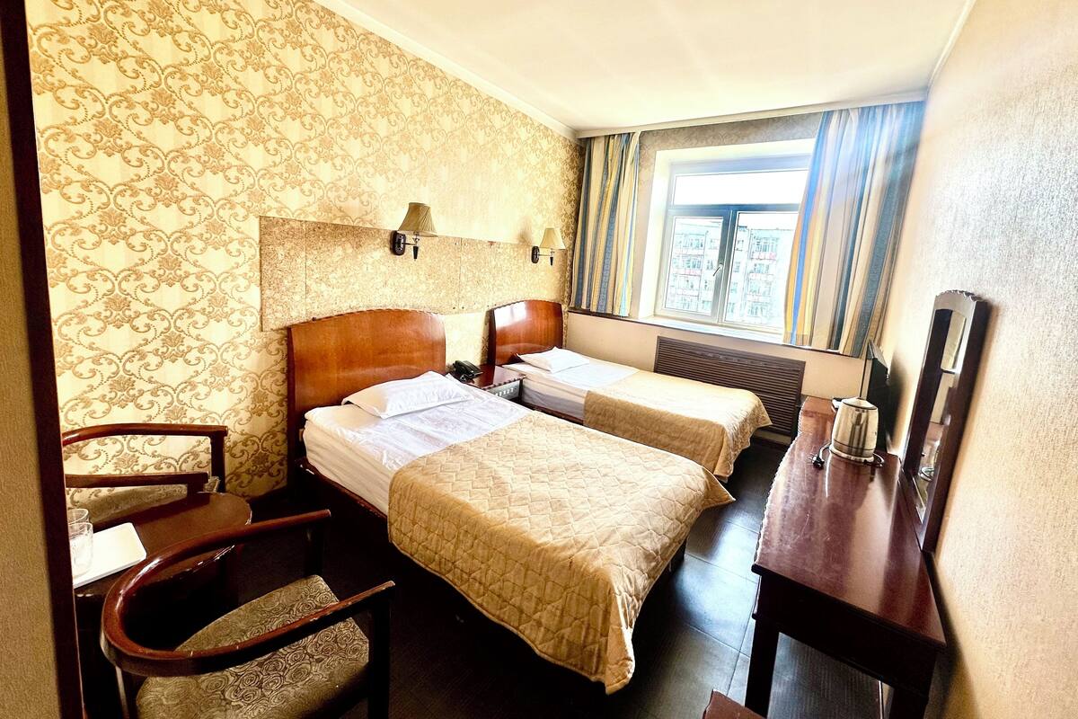 A hotel room with two beds, a desk, a chair, a lamp, and a window with curtains.