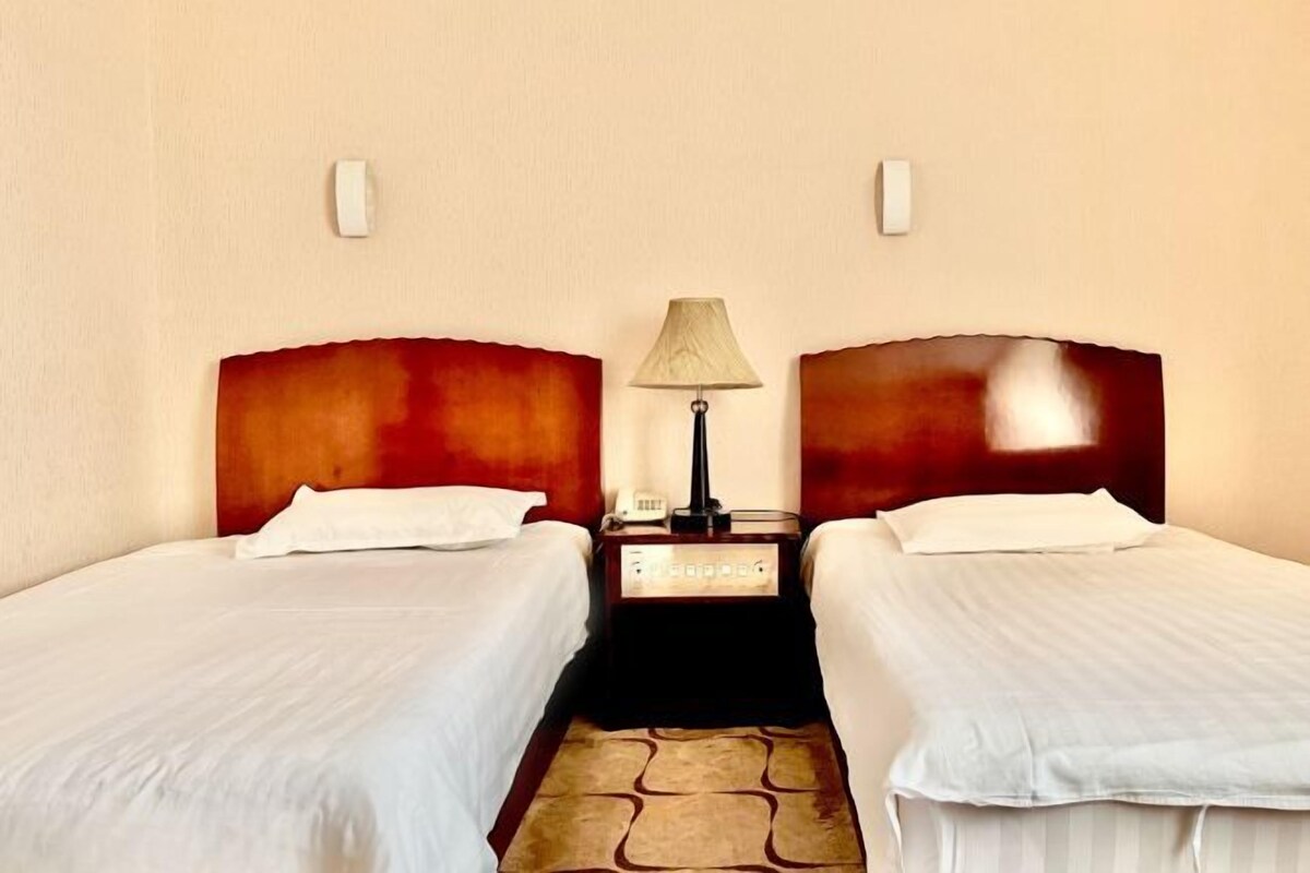 A hotel room with two single beds, a nightstand with a lamp, and a telephone.