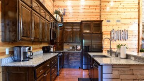 A kitchen with wooden cabinets, granite countertops, a refrigerator, and a stone accent wall.