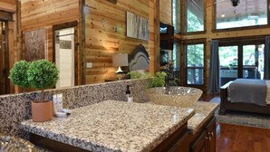 A bathroom with granite countertops, a large mirror, a potted plant, and a glass bowl sink.