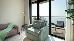 Un salon moderne avec un canapé, un fauteuil vert et une vue sur la mer grâce à de grandes fenêtres.