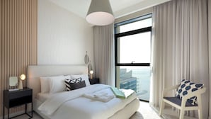 Une chambre moderne avec un grand lit, une table de chevet, une commode, une chaise et une vue sur la ville grâce à une grande fenêtre.