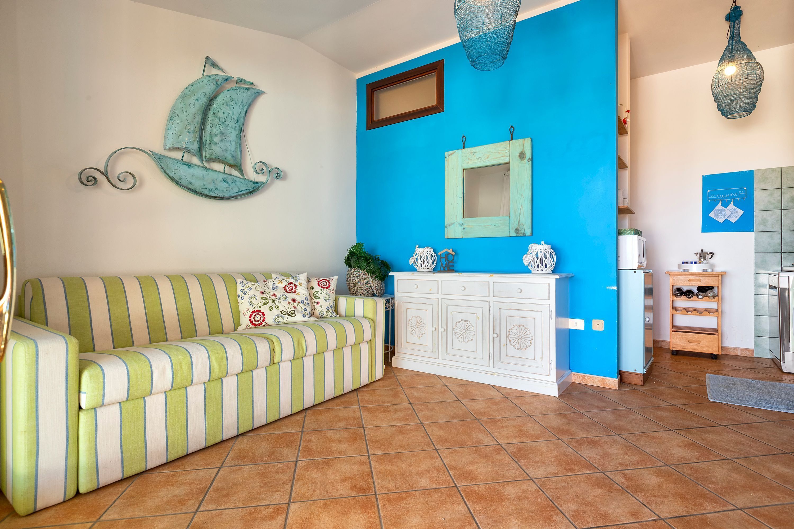 Una sala de estar con un sofá a rayas, un aparador blanco, una pared azul y una lámpara colgante.