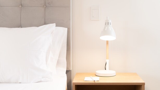 A neatly made bed with white linens and a grey headboard. A white desk lamp is on a wooden nightstand beside the bed. - w Cozy Loft With Fantastic View in El Poblado (Medellín)