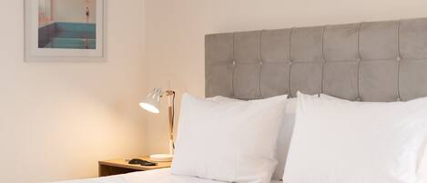 A neatly made bed with white linens, a grey tufted headboard, and a bedside table with a lamp and a phone.