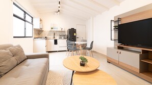 Ein modernes Wohnzimmer mit einer Couch, einem runden Holztisch, einem Fernseher und einem Essbereich mit Stühlen und einem Tisch.