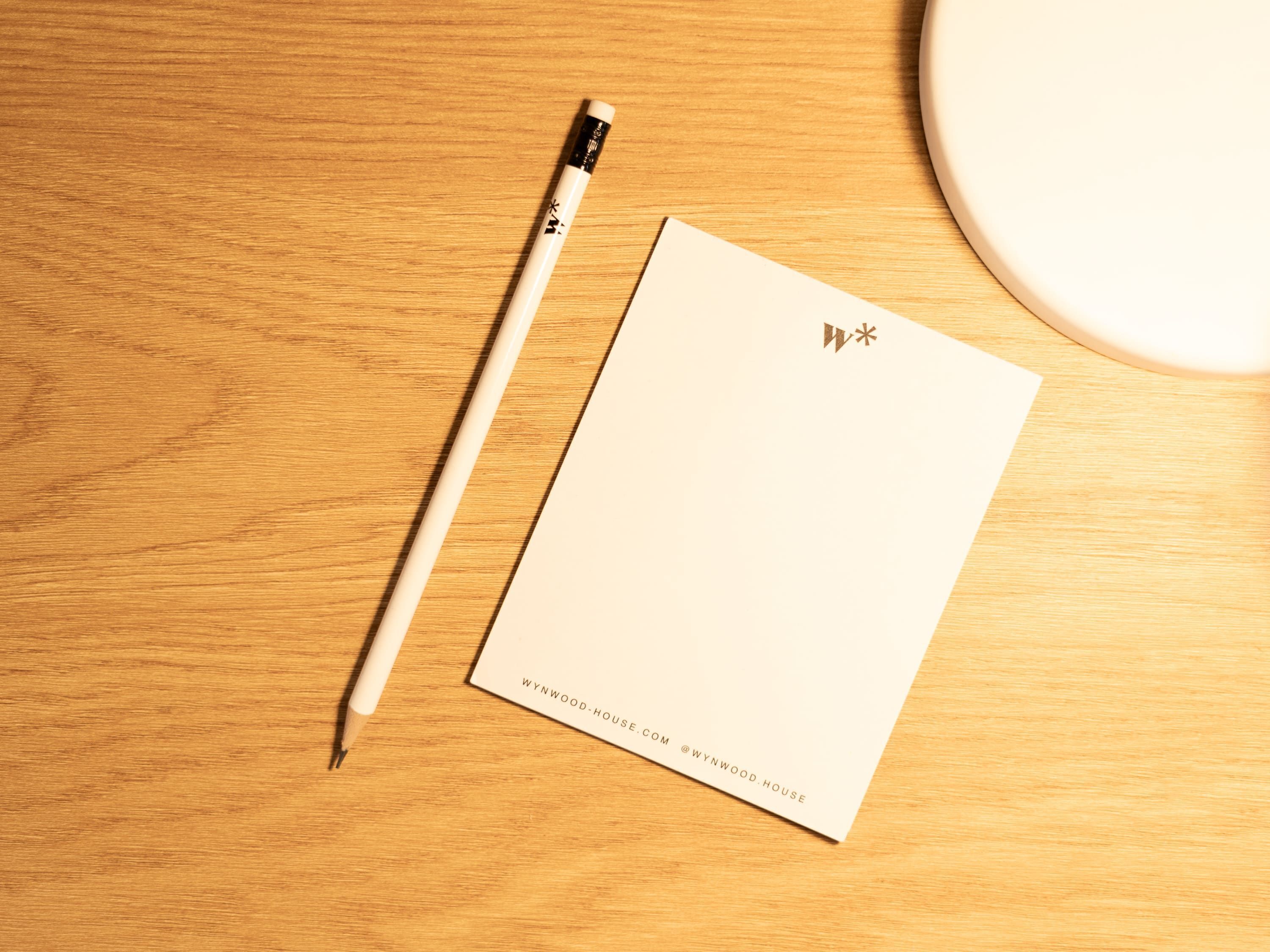 A wooden desk with a white notepad, a pencil, and a circular object.