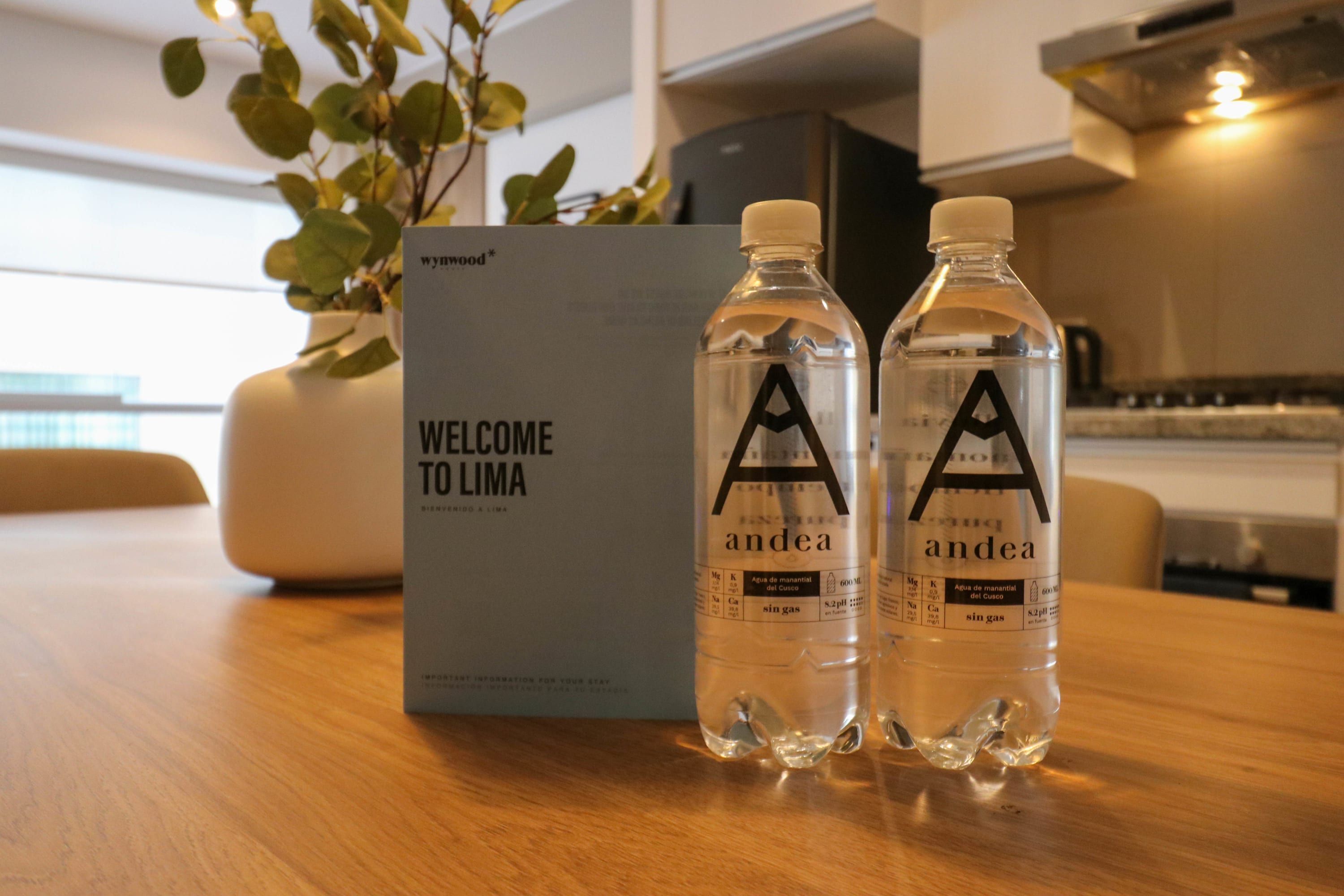Twee waterflessen met 'andea' branding op een houten tafel naast een bord met de tekst 'WELCOME TO LIMA'.