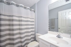 A bathroom with a striped shower curtain, a white toilet, and a white sink with a mirror above it.