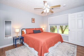 A bedroom with a bed, nightstand, ceiling fan, window, and door.