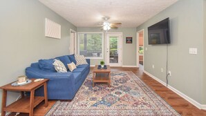 A living room with a blue sofa, a patterned rug, a ceiling fan, and a television on the wall.
