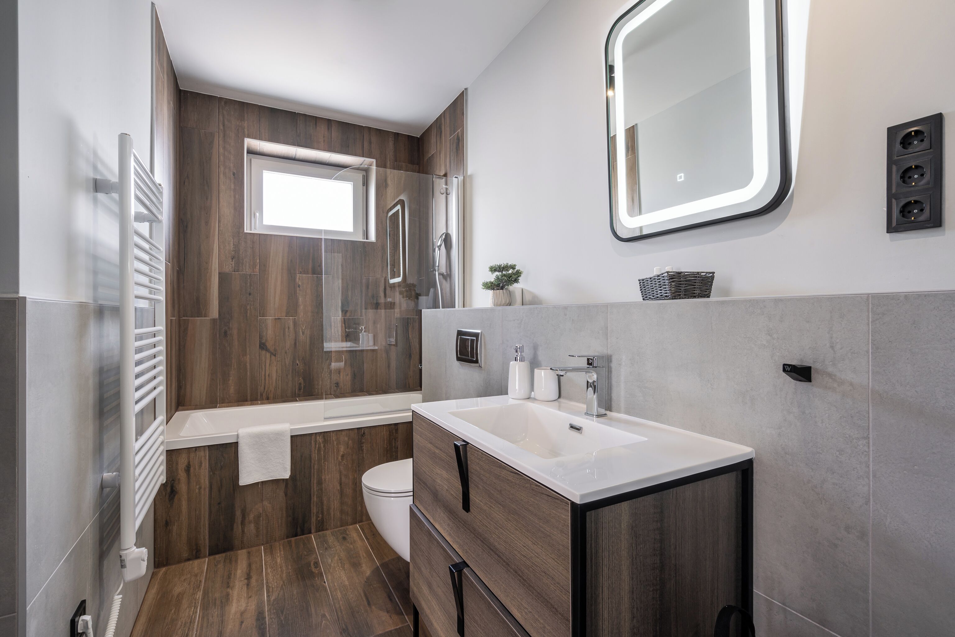 A modern bathroom with a wooden vanity, a bathtub, and a large mirror.