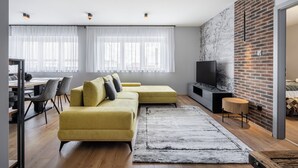 A modern living room with a yellow sofa, a TV, and a brick accent wall. - Radnoti Home (Veszprem)