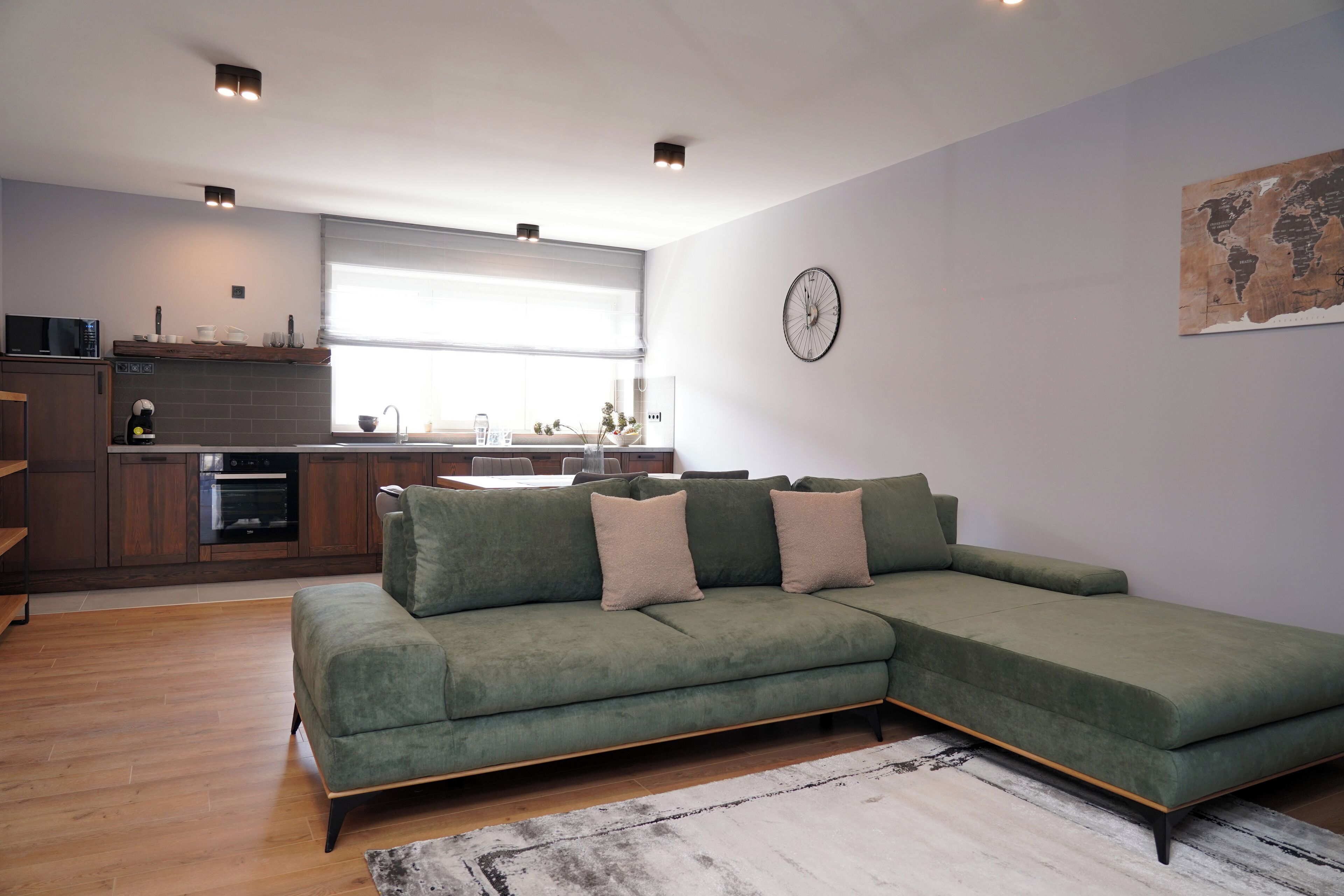 A modern living room with a sectional sofa, a kitchen area with a window, and a world map on the wall.