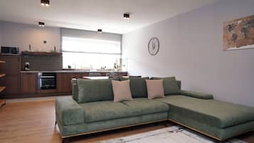 A modern living room with a sectional sofa, a kitchen area with a window, and a world map on the wall.