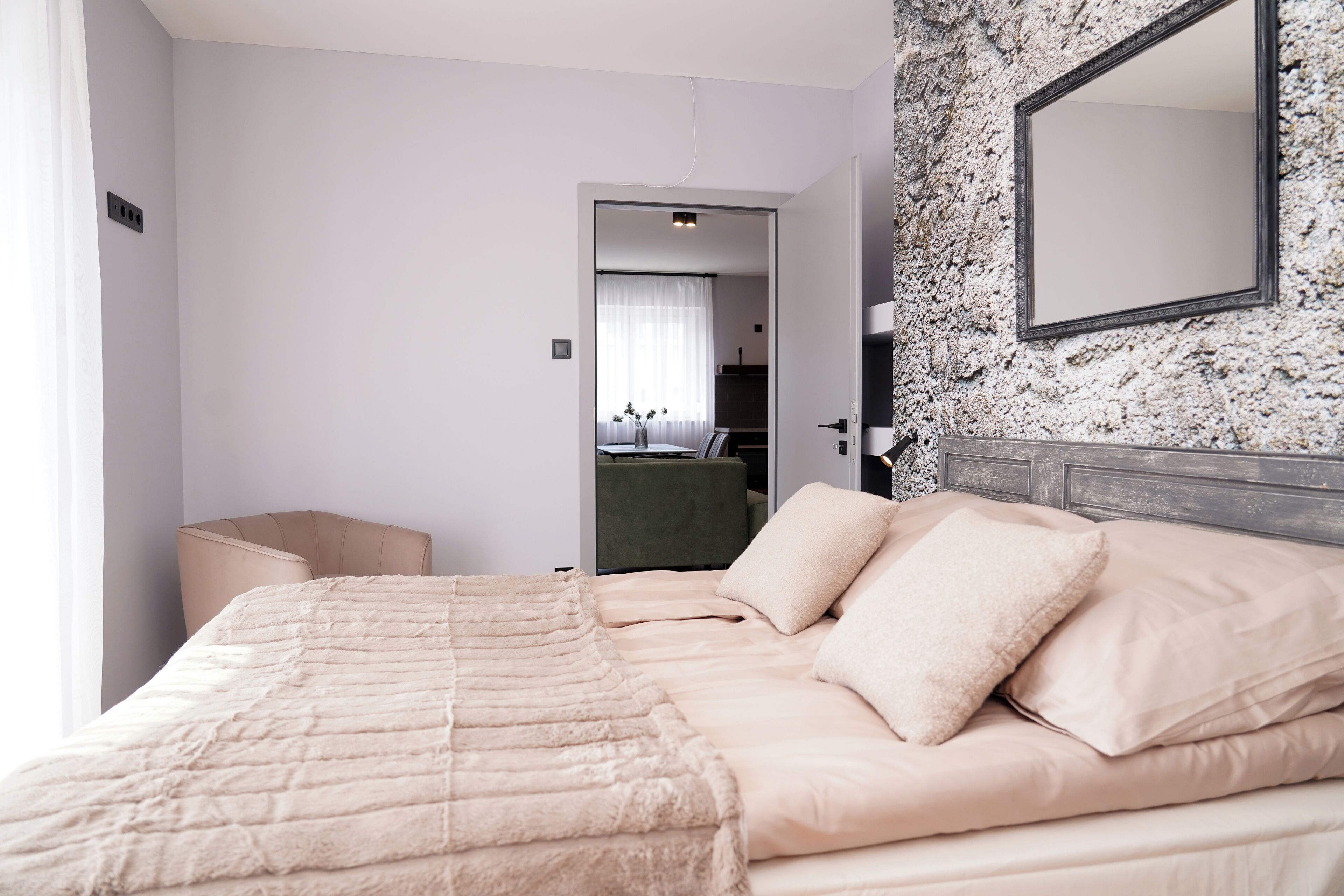 Habitación de hotel con una cama grande, cabecero, espejo y vista a la habitación contigua.