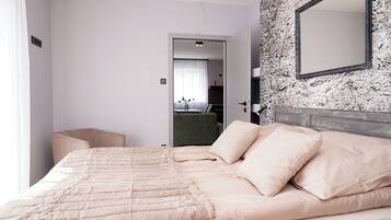 Habitación de hotel con una cama grande, cabecero, espejo y vista a la habitación contigua.