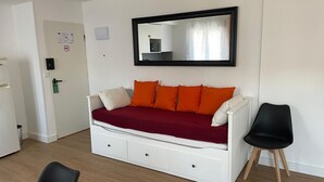 A room with a white sofa bed, orange cushions, a black chair, and a mirror on the wall.