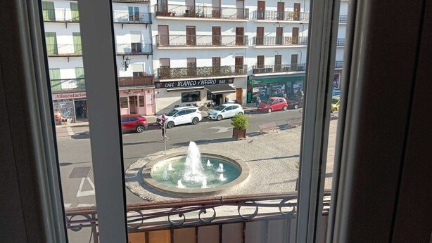A view of a street with a fountain, cars, and buildings including a bar named "Blanco y Negro".