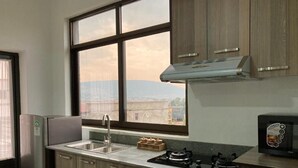A modern kitchen with a large window, stainless steel appliances, and wooden cabinets. - Rebero View Apartments (Kigali)