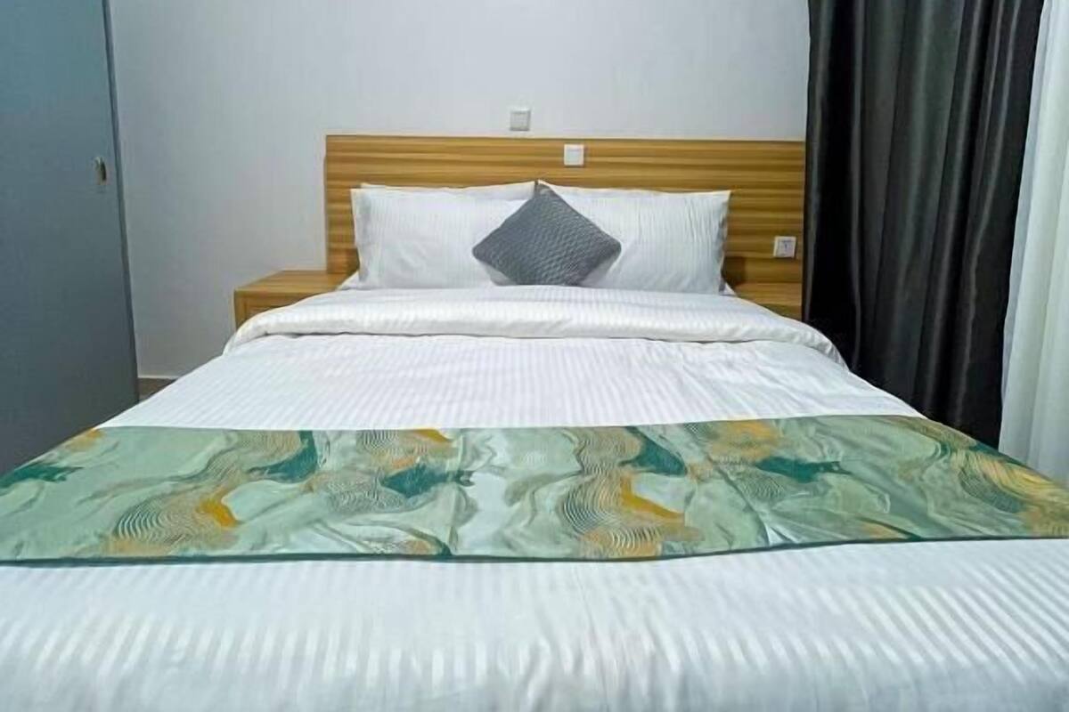 A single bed with a wooden headboard, white bedding, and a patterned throw blanket.